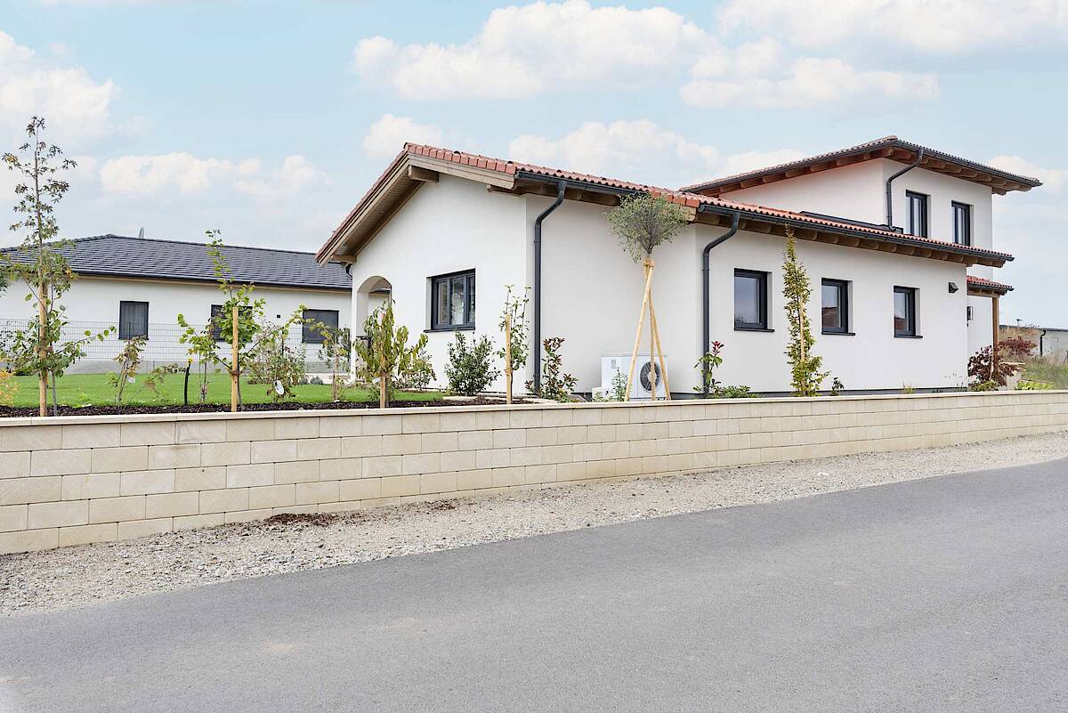 Außenansicht des Hauses mit einem niedrigen Zaun, grüner Begrünung und moderner weißer Fassade.