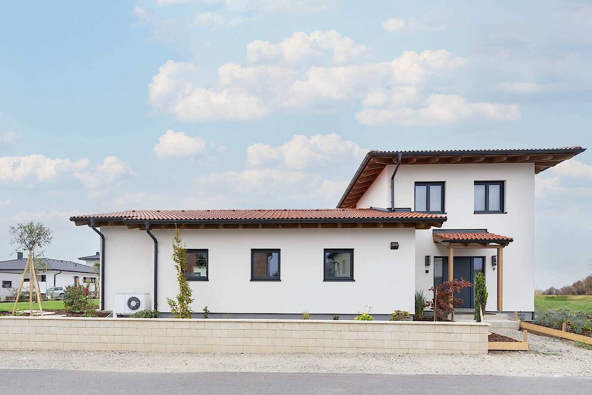 Außenansicht eines modernen Hauses mit roten Dachziegeln und weißer Fassade, eingefasst von einem gepflegten Garten.