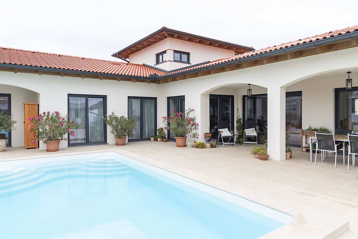 Außenbereich eines Hauses mit großzügiger Terrasse und Pool, umgeben von Pflanzen und modernen Glasschiebetüren.