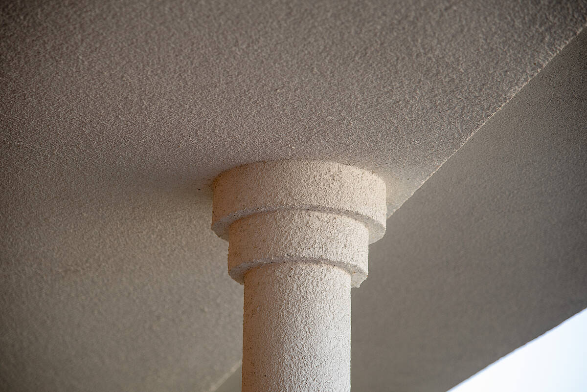 Architekturdetail einer Säule: Nahaufnahme einer strukturierten Säule mit einer groben Oberfläche, die das Dach einer überdachten Terrasse stützt.