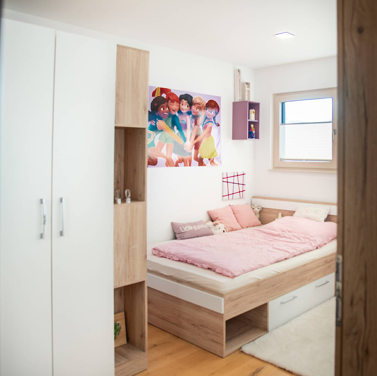 Kinderzimmer mit pinker Bettwäsche: Helles Kinderzimmer mit Holz- und Weißtönen. Ein Einzelbett mit pinker Bettwäsche und farbenfroher Wanddekoration.