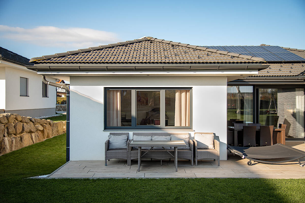 Vorderansicht eines Bungalow Einfamilienhauses mit Sitzbereich auf der Terrasse.