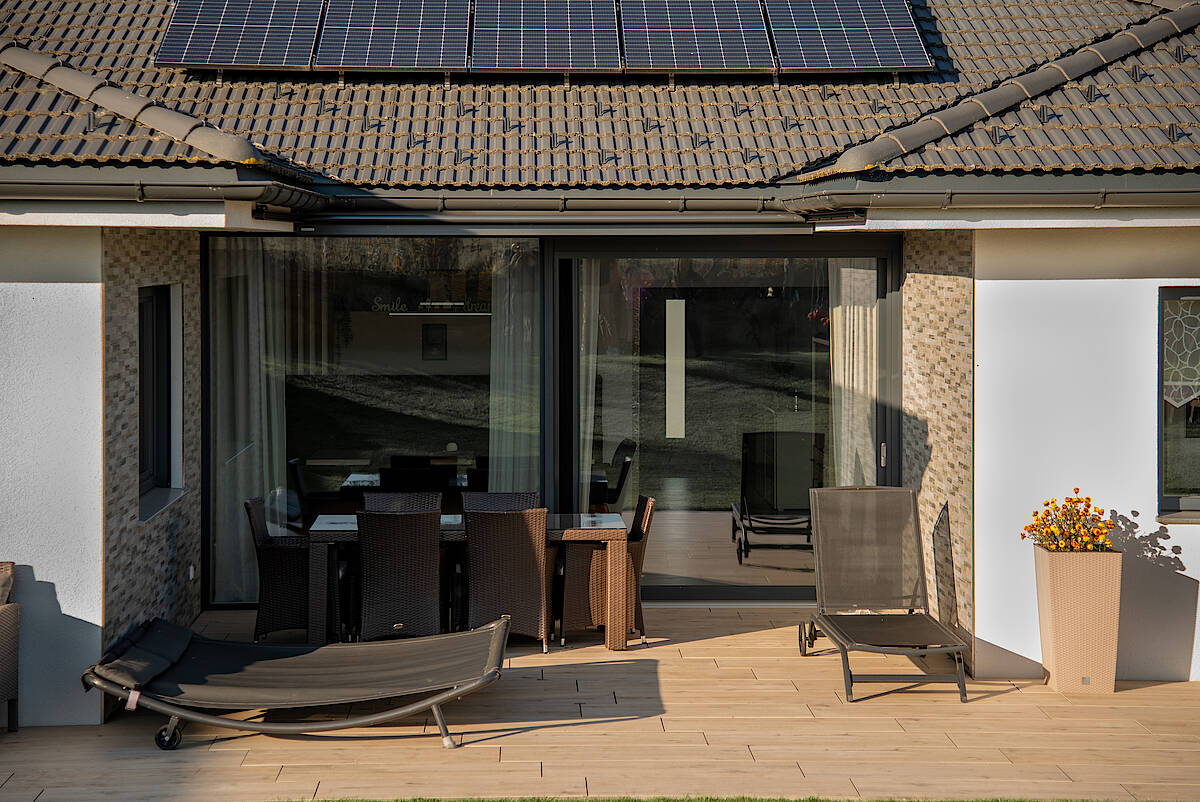 Terrassenansicht eines Bungalows mit Solarpanelen und Gartenmöbeln.